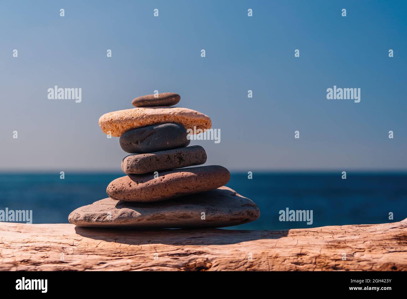 Equilibrata piramide di ciottoli sulla spiaggia in una giornata di sole. Abstract Sea bokeh sullo sfondo. Messa a fuoco selettiva. Pietre Zen sulla spiaggia di mare, meditazione Foto Stock