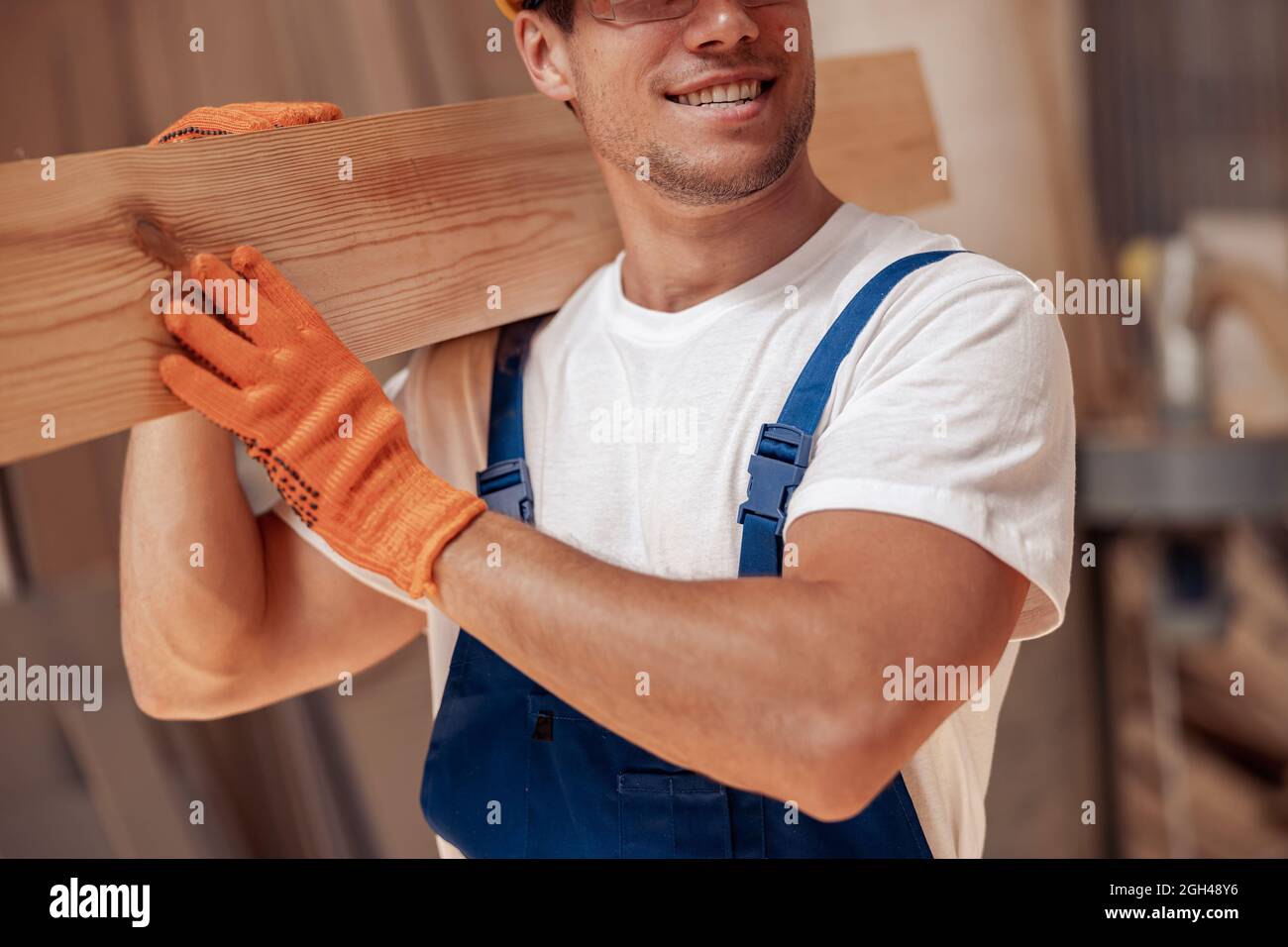 Gioioso lavoratore che trasporta legno asse in cantiere Foto Stock