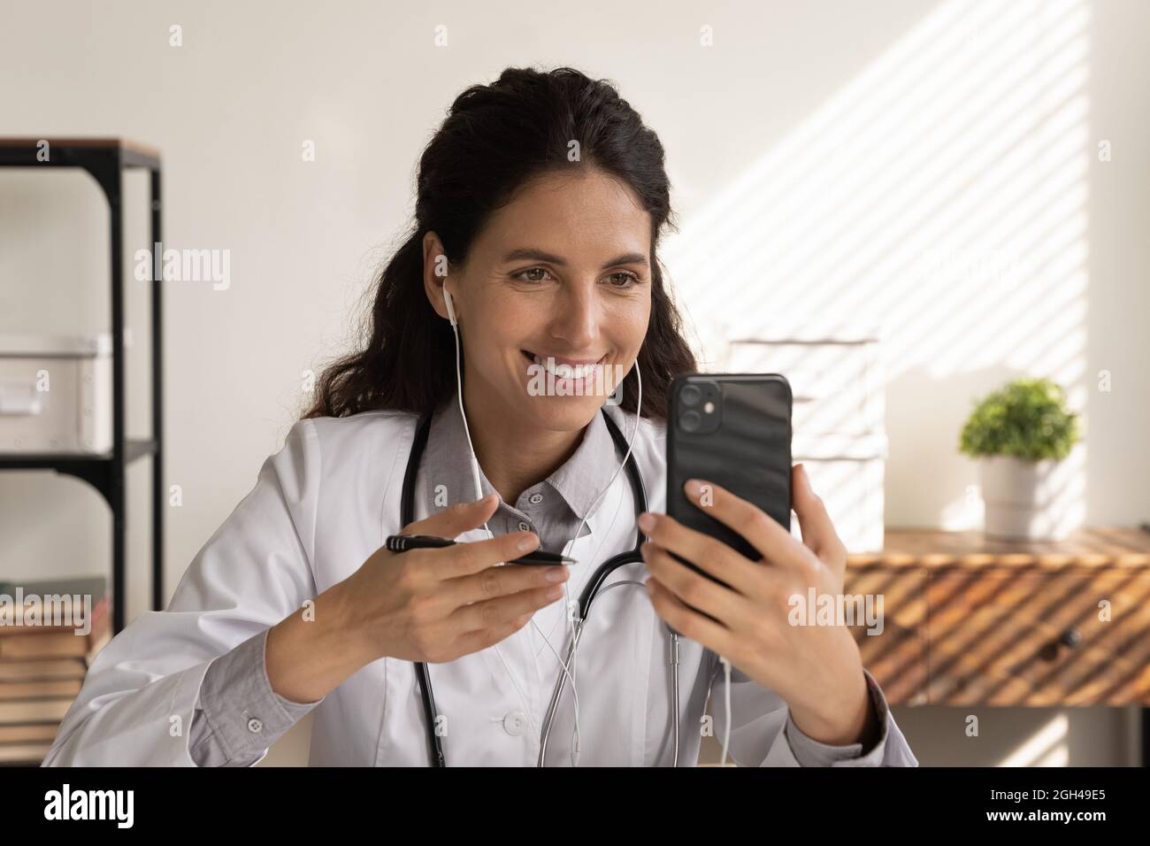 Felice medico donna focalizzato in auricolari utilizzando il telefono cellulare Foto Stock