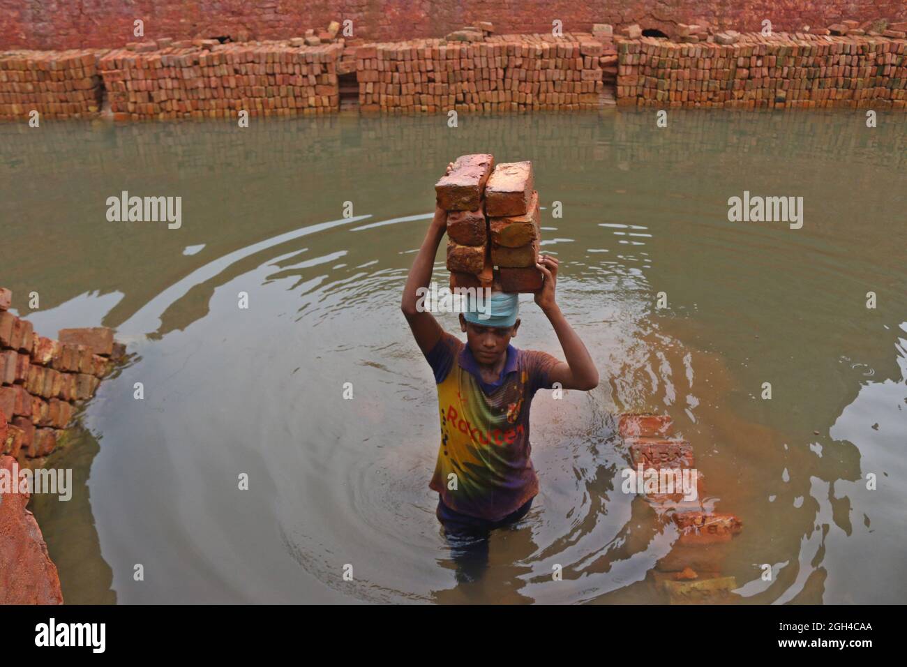 Non esclusiva: DHAKA, BANGLADESH- 4 SETTEMBRE: Un uomo tiene i mattoni sulla sua testa dopo averli sfornati, mentre lei attraversa il fiume su un pla Foto Stock