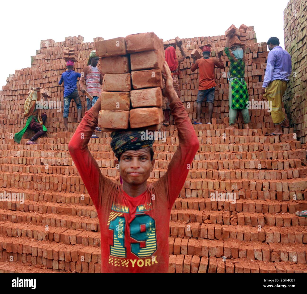 Non esclusiva: DHAKA, BANGLADESH- 4 SETTEMBRE: Un uomo tiene i mattoni sulla sua testa dopo averli sfornati, mentre lei attraversa il fiume su un pla Foto Stock