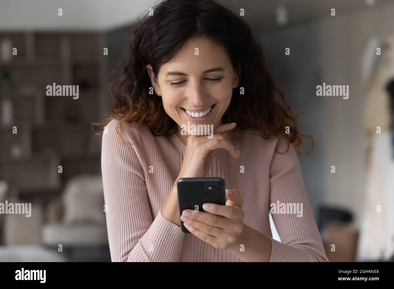 Felice giovane donna latina che usa il cellulare a casa. Foto Stock