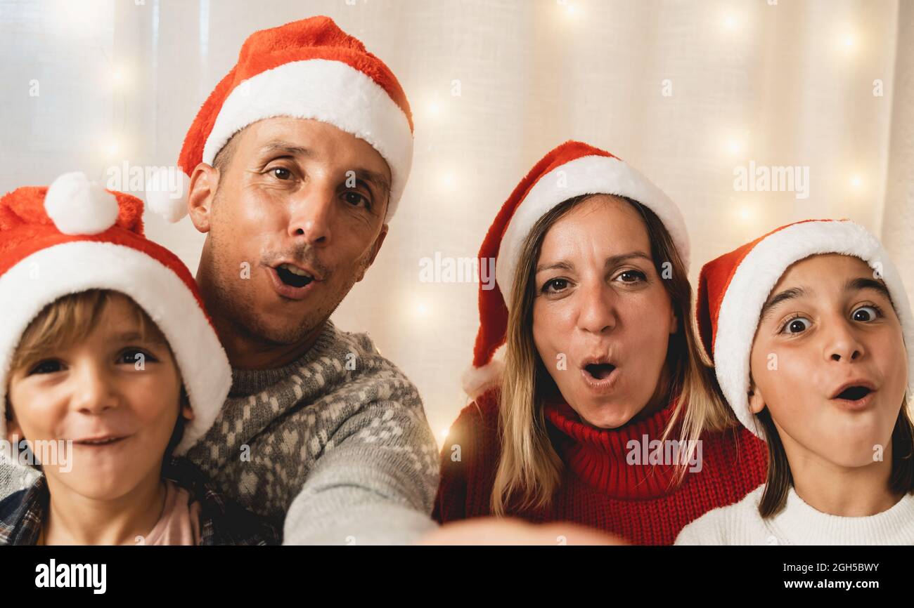 Famiglia felice che fa selfie con il telefono mobile che indossa i cappelli di Santa Clause durante la vigilia di Natale - fuoco sulla faccia della madre Foto Stock