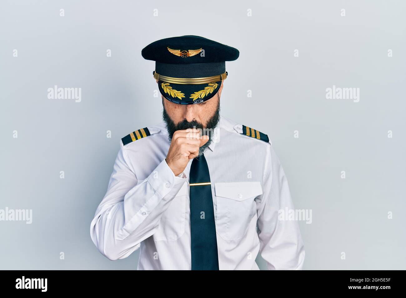 Giovane uomo ispanico che indossa un aereo pilota uniforme sensazione di malessere e tosse come sintomo di raffreddore o bronchite. Concetto di assistenza sanitaria. Foto Stock