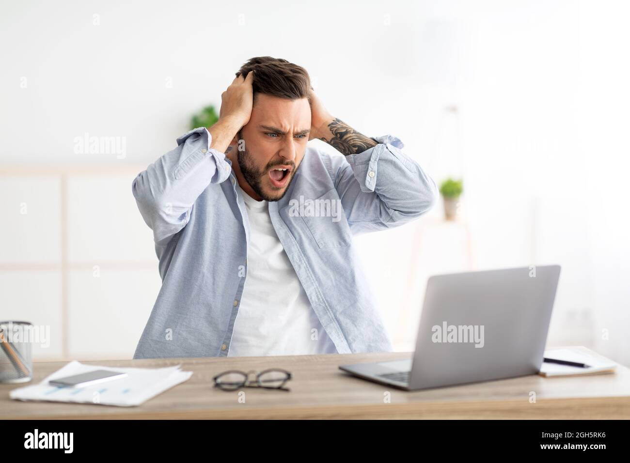 Uomo arrabbiato che ha software, errore di sito web, guardando lo schermo del laptop e gesturing, seduto sul posto di lavoro in casa interni Foto Stock