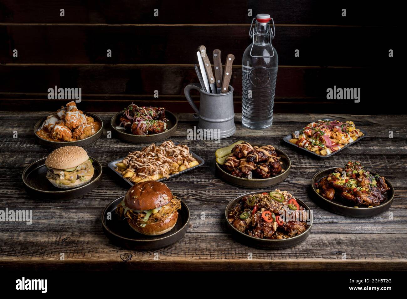Servito tavolo in legno con appetitosi hamburger e ali di pollo nel ristorante di Street food Foto Stock
