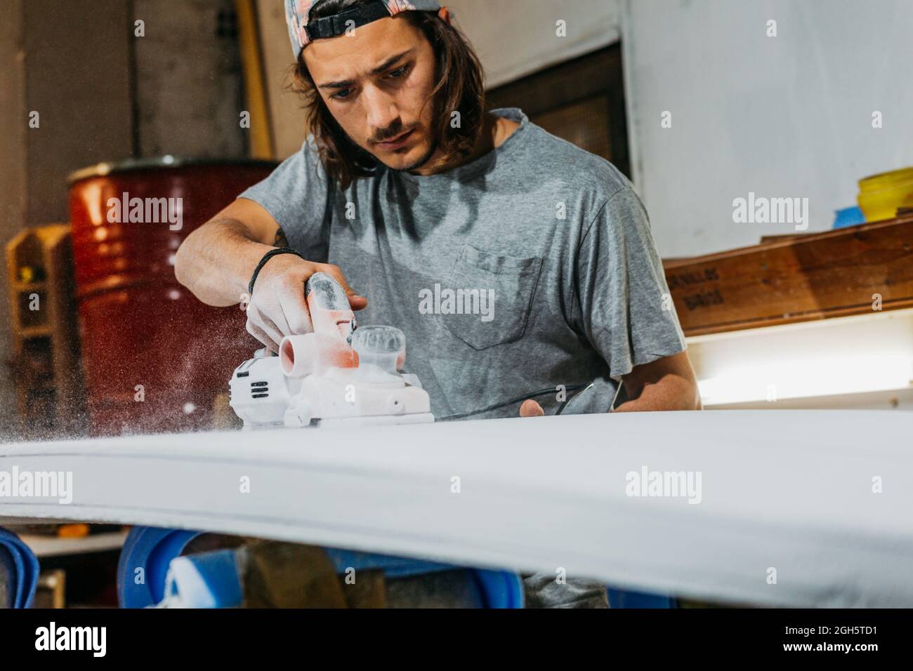 Formatore maschio che utilizza la spianatrice elettrica e la superficie di lucidatura della tavola da surf in officina Foto Stock