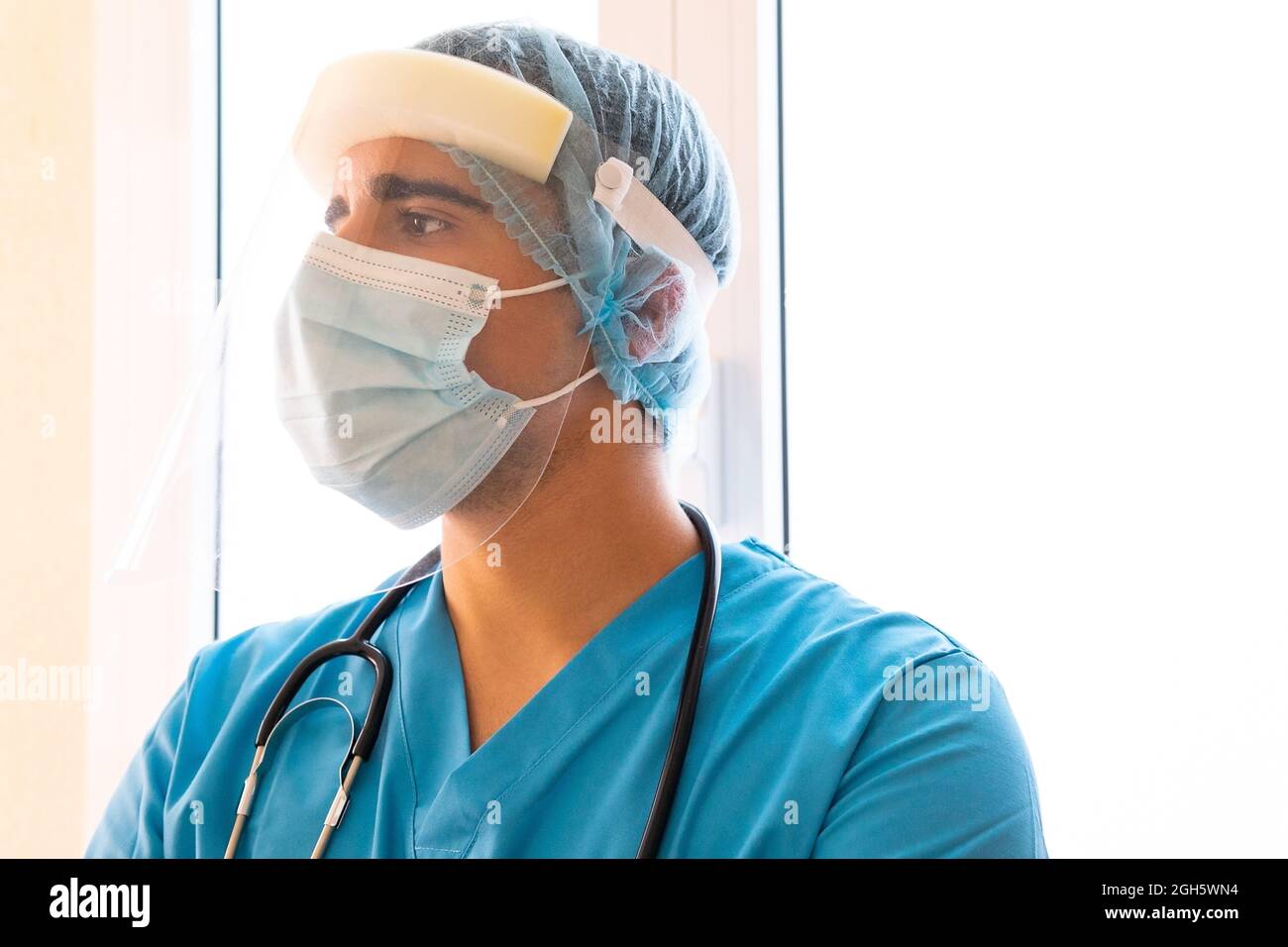 Medico maschio con protezione del viso in plastica mentre si lavora in clinica e guardando via Foto Stock