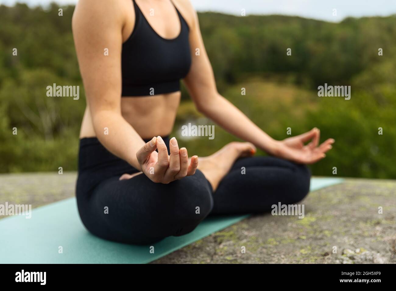 Anonimo giovane donna che chiude gli occhi mentre meditating in posa del loto sulla pietra in campagna Foto Stock