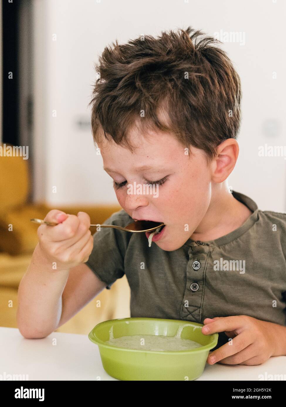 Adorabile ragazzo mangiando appetitosa zuppa di panna con cucchiaio durante il pranzo a casa Foto Stock