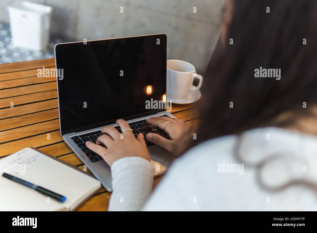 La giovane studentessa latino-americana, dal taglio irriconoscibile, legge le informazioni sullo schermo del computer portatile mentre si prepara per l'esame universitario in un accogliente bar Foto Stock