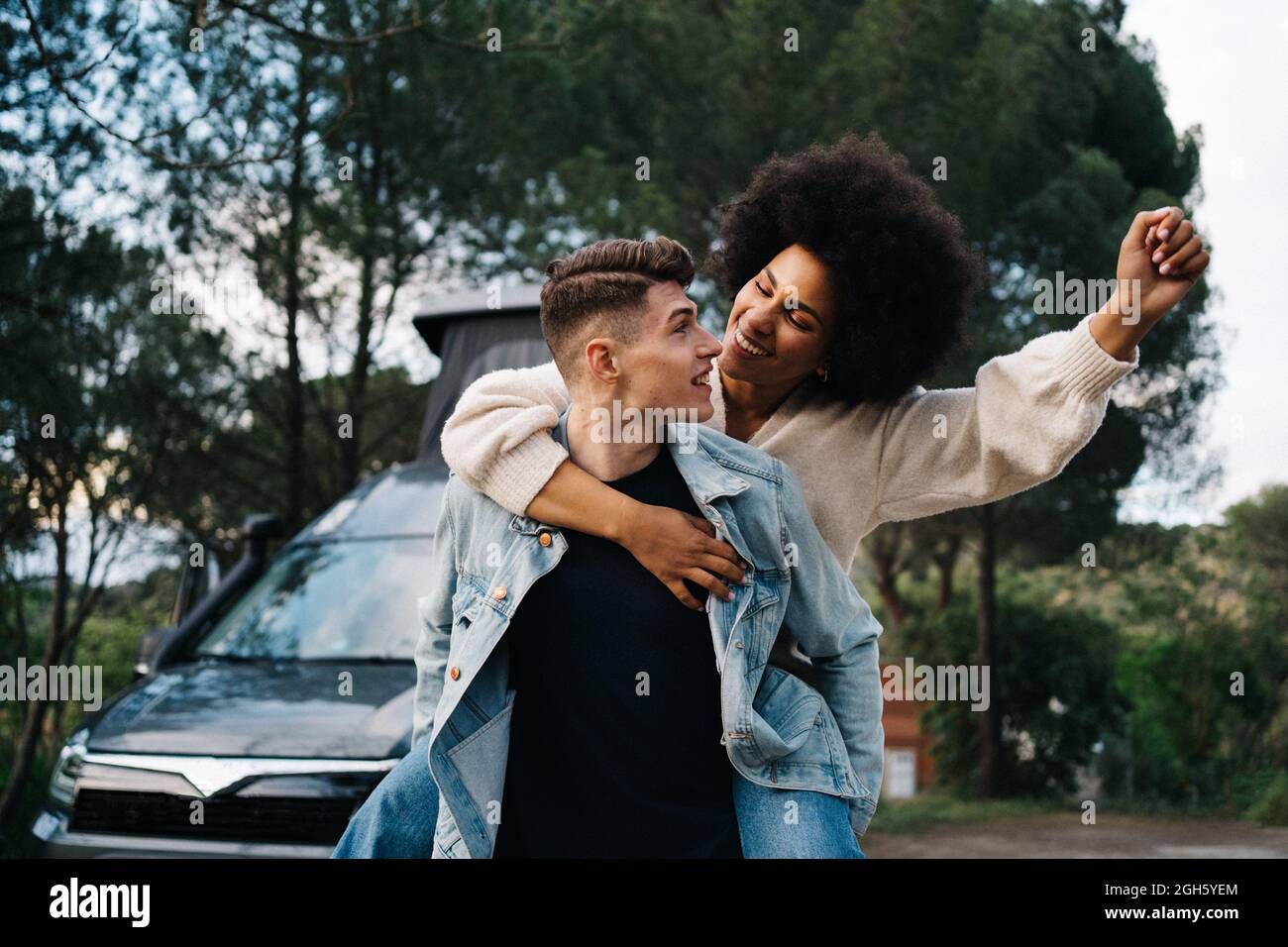 Giovane uomo che dà allegro etnia ragazza Piggyback giro contro camper e Thai Ridgeback sul sentiero Foto Stock