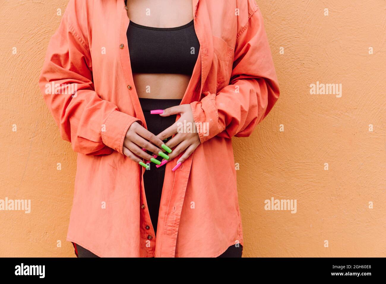 Naughty femmina che mostra la lingua mentre copre gli occhi con le mani con lunghe unghie luminose su sfondo arancione Foto Stock