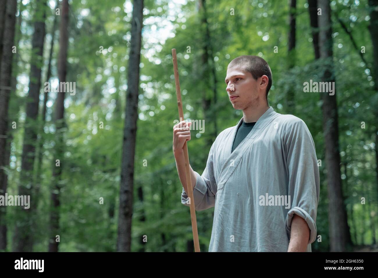 uomo con bastone che tiene la mano vicino al petto mentre pratica kung fu in bosco Foto Stock