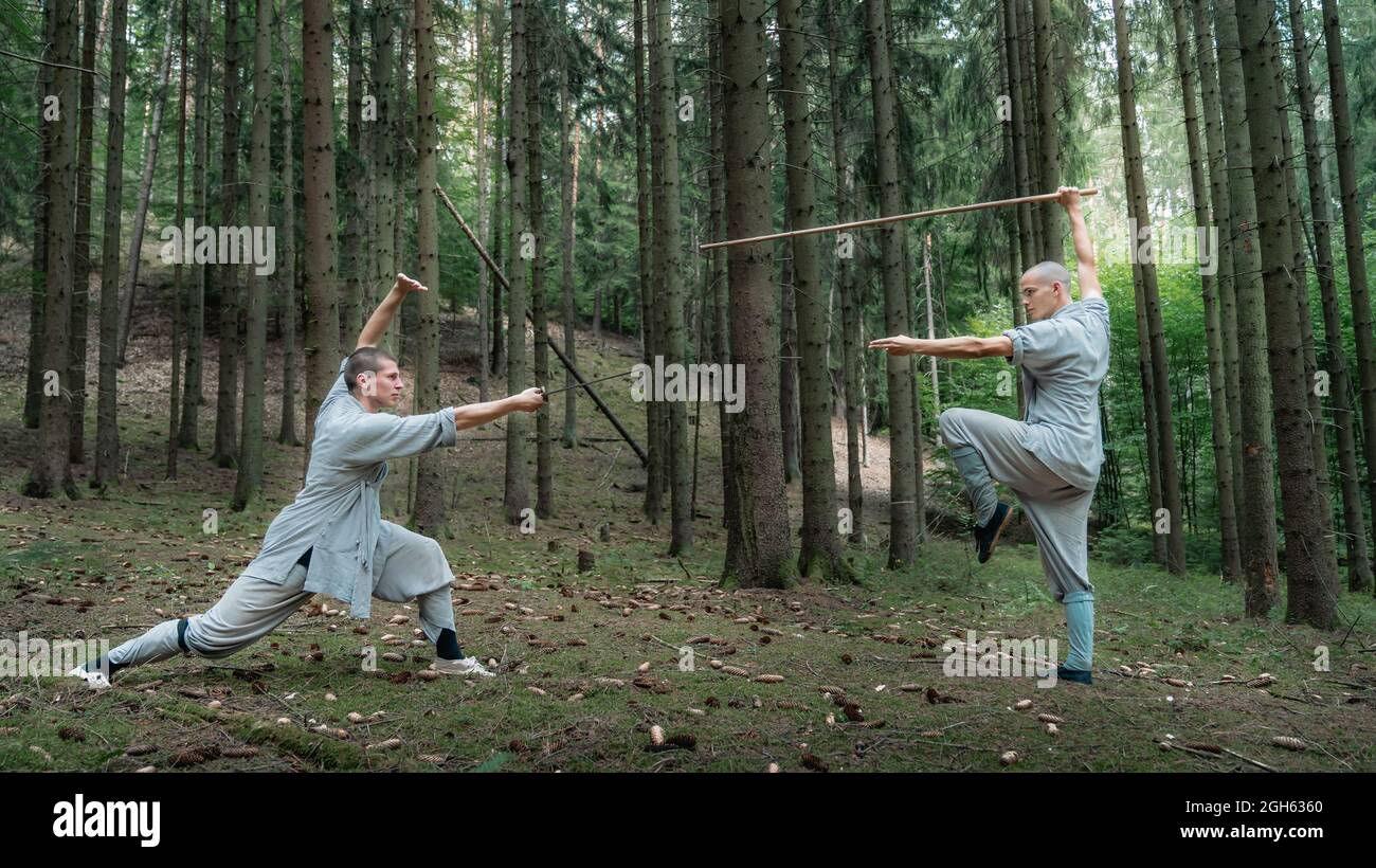 Uomini a corpo pieno in abiti grigi praticando kung fu con bastone e spada durante l'allenamento in legno Foto Stock