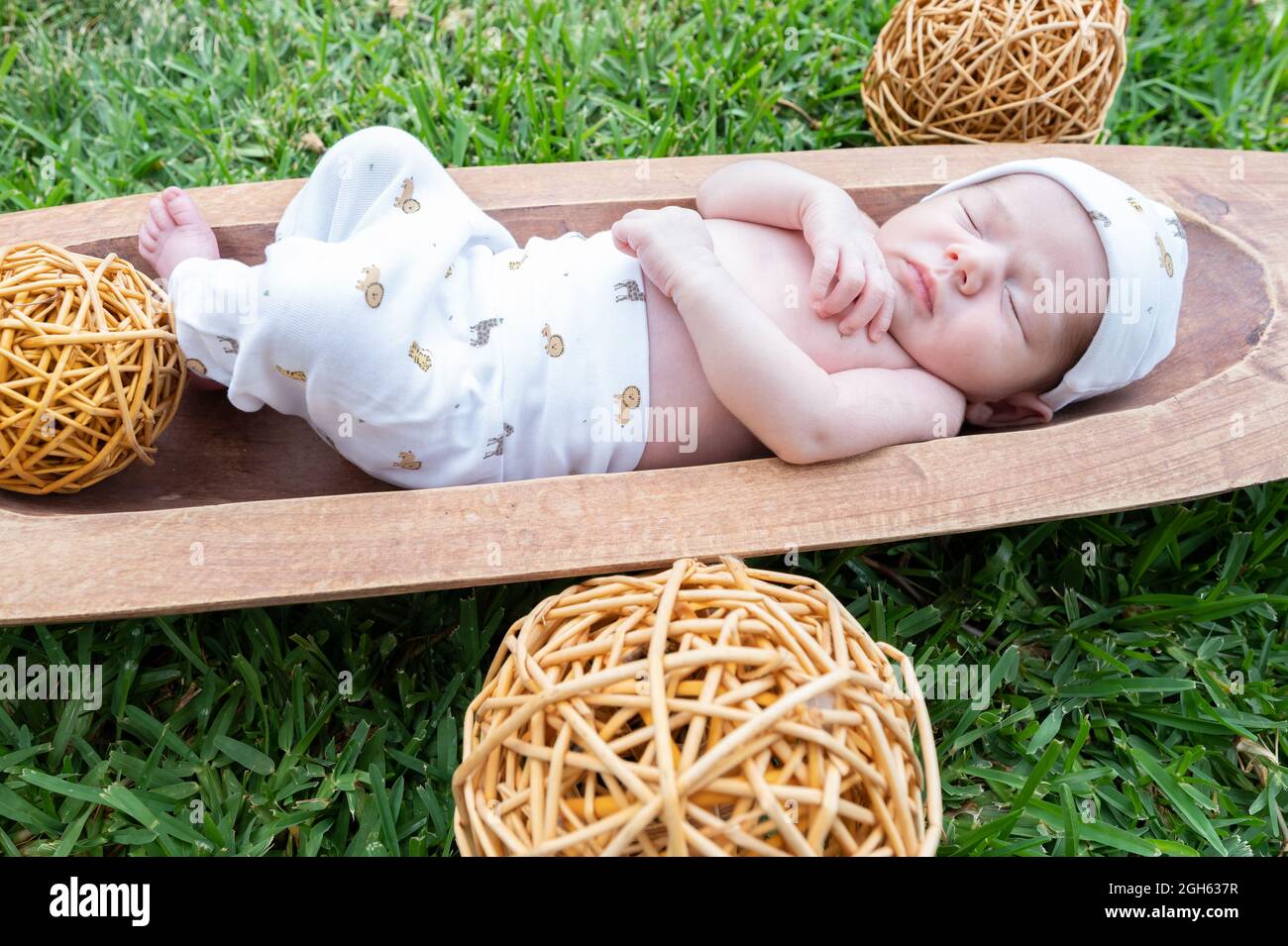 Carino piccolo neonato che dorme mentre si trova in vasca di legno posto su erba verde Foto Stock