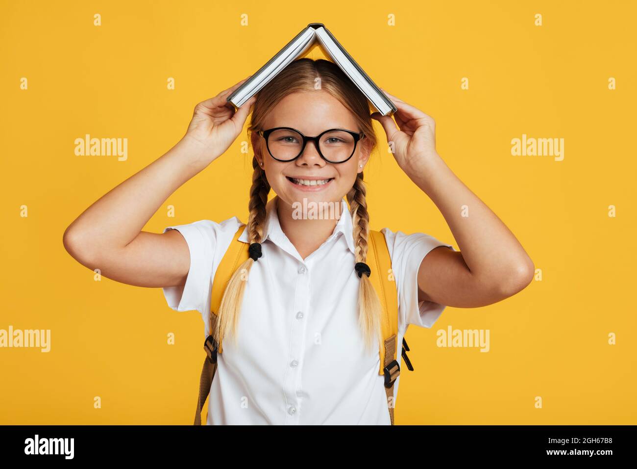 Felice ragazza bionda giovane caucasica carina in occhiali tenendo libro sulla sua testa Foto Stock