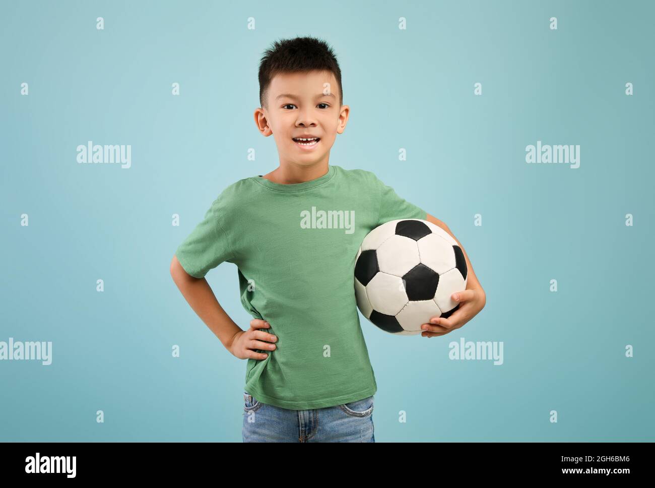 Felice ragazzo asiatico con pallone da calcio in mano su sfondo blu Foto Stock