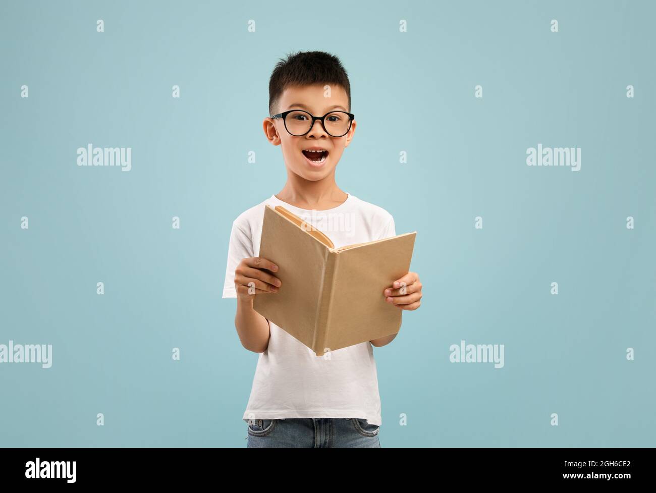 Ragazzo asiatico giovane eccitato che indossa occhiali tenendo e leggendo libro aperto Foto Stock