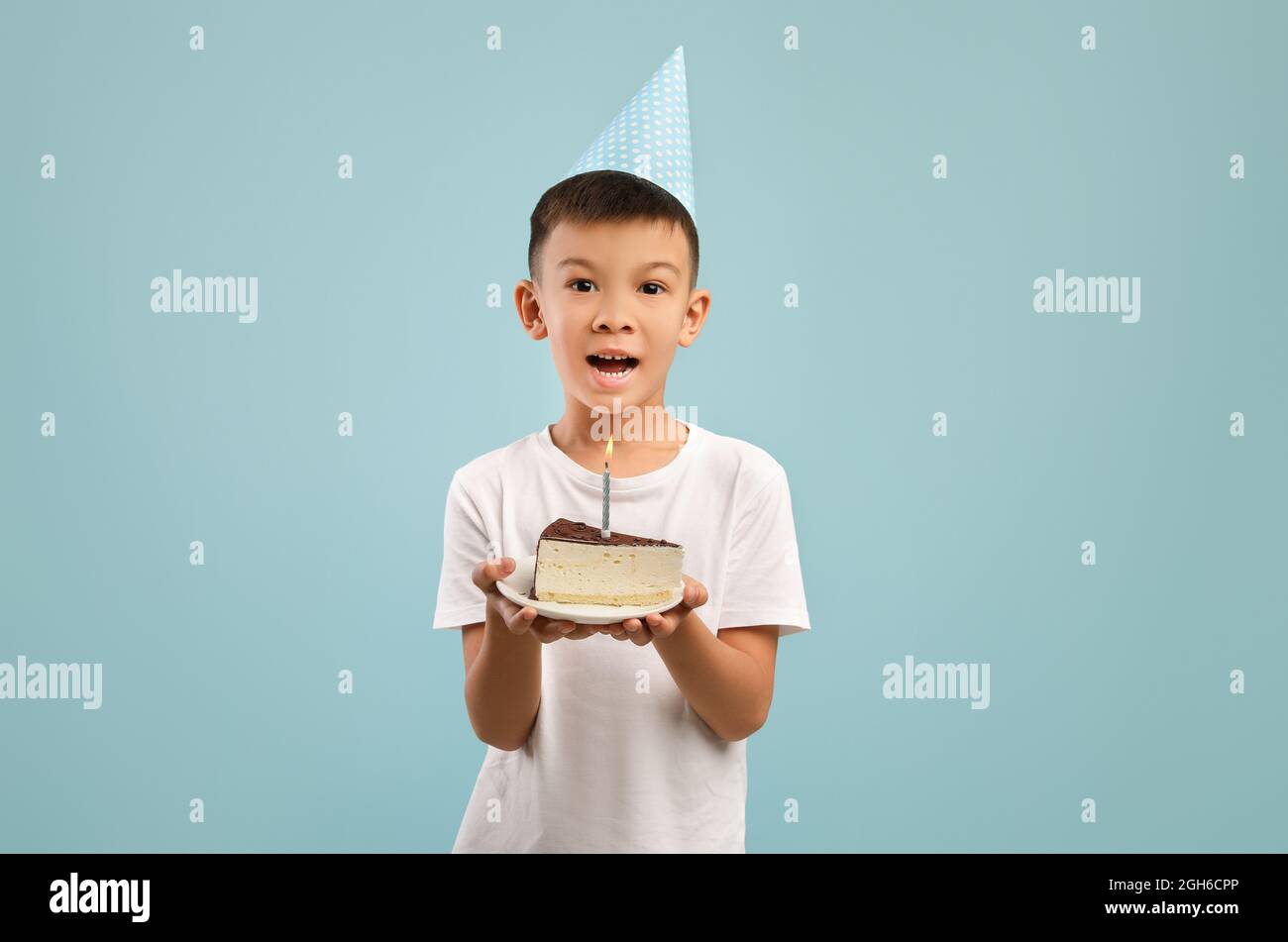 Happy Little Asian Boy in Party Hat Holding torta di compleanno con candela Foto Stock