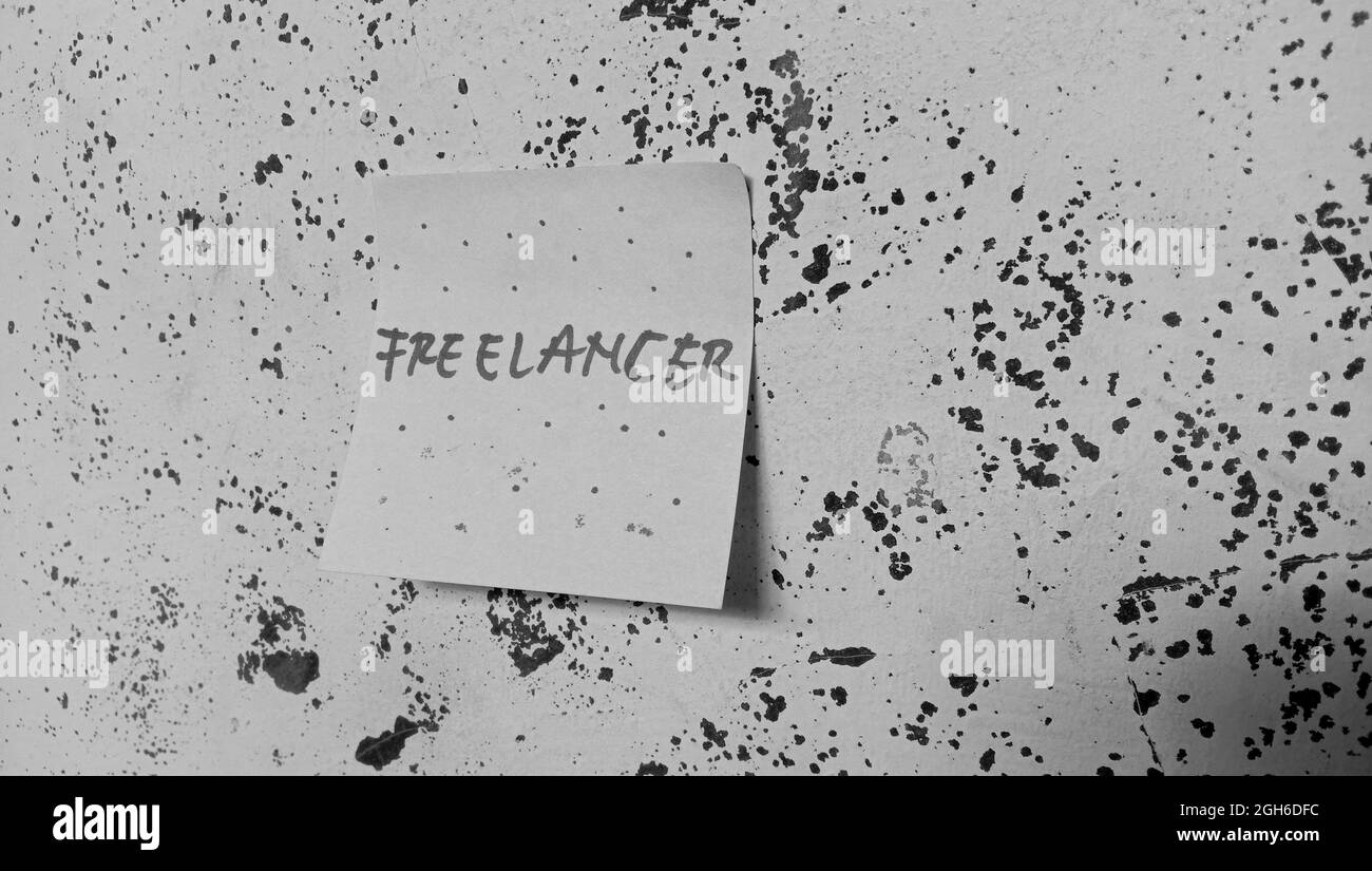 Una carta con un 'freelance' scritto su di essa applicata a una parete danneggiata in scala di grigi Foto Stock