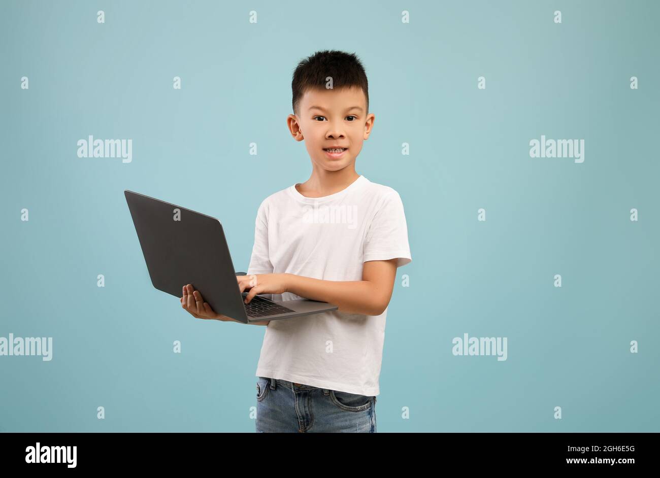 Concetto di formazione online. Piccolo ragazzo asiatico con laptop in posa su sfondo blu Foto Stock