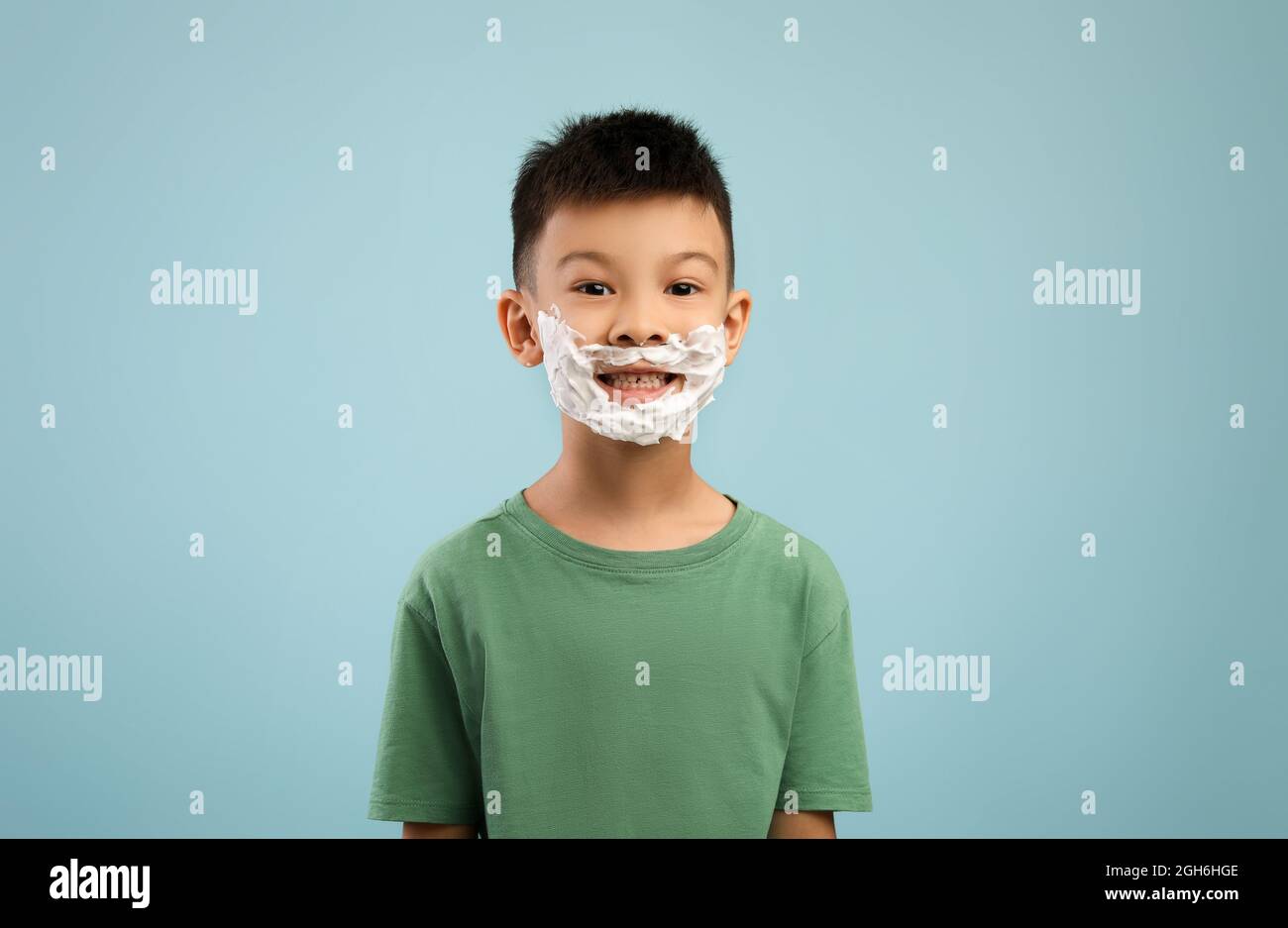 Ragazzo asiatico con schiuma da barba sul viso che posa su sfondo blu Foto Stock