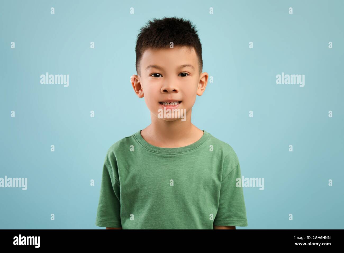 Ritratto di ragazzo asiatico in t-shirt verde posato su sfondo blu Foto Stock