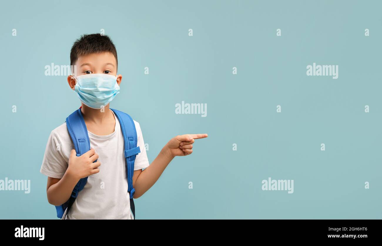 Controllare. Ragazzo asiatico che indossa maschera medica e zaino puntato da parte Foto Stock