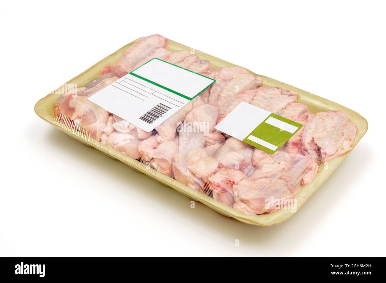 Ali di pollo crude confezionate in un piatto di polistirolo con un'etichetta su sfondo bianco. Foto Stock