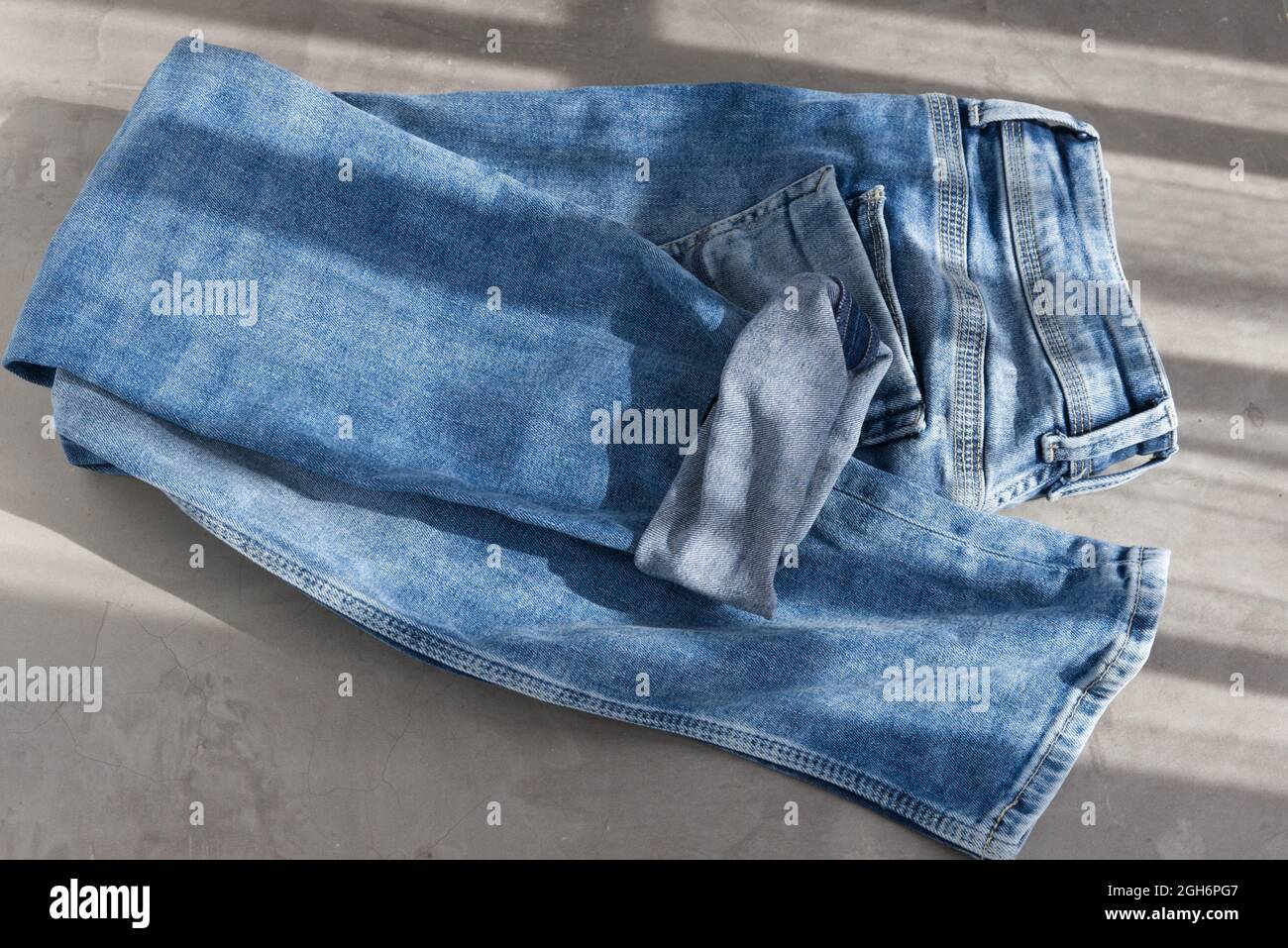 jeans piegati in blu su sfondo grigio. Luce solare Foto Stock