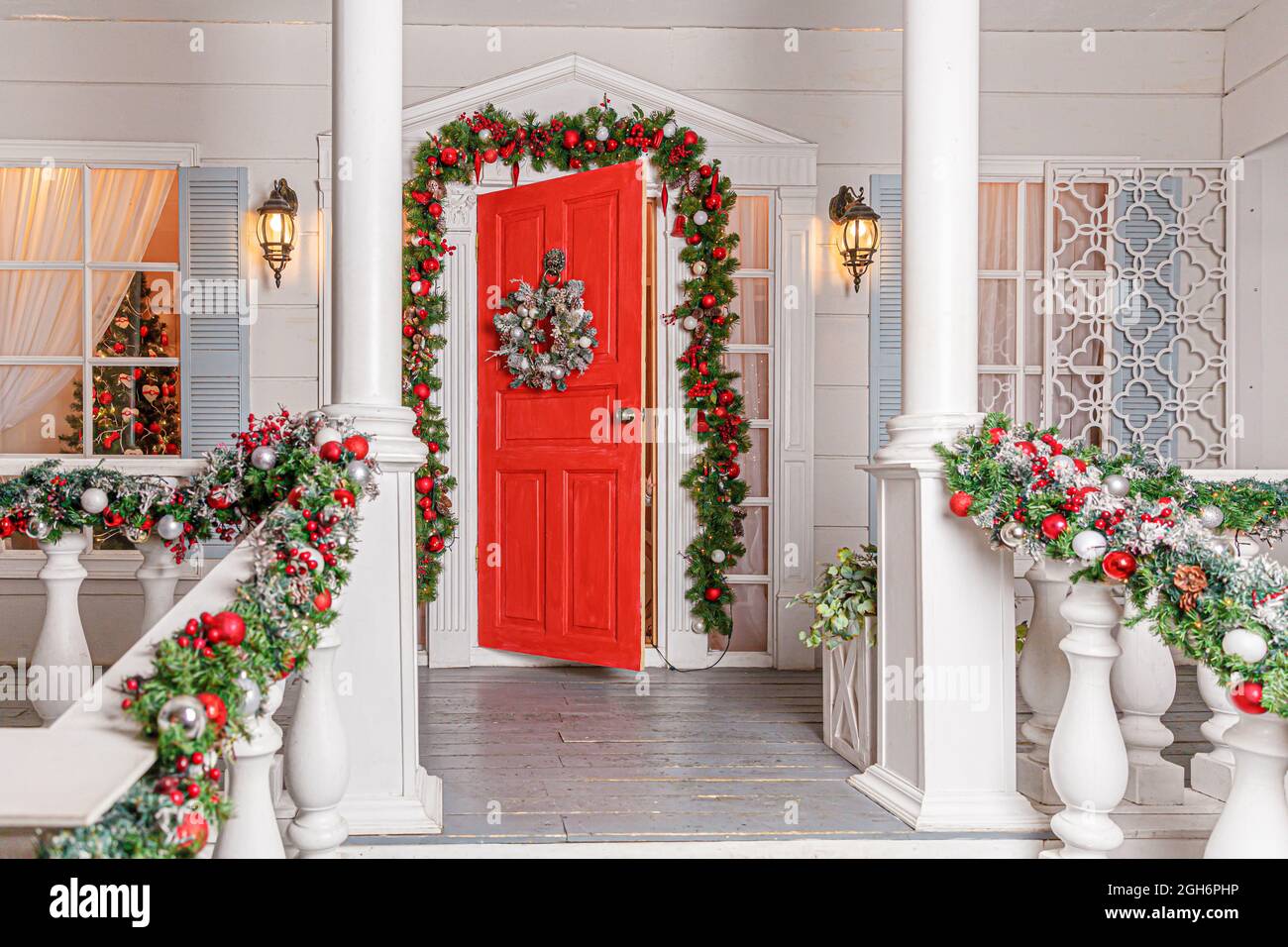 Idea decorazione portico di Natale. Ingresso casa con porta rossa decorata  per le vacanze. Corona rossa e verde di rami di abeti e luci accese Foto  stock - Alamy