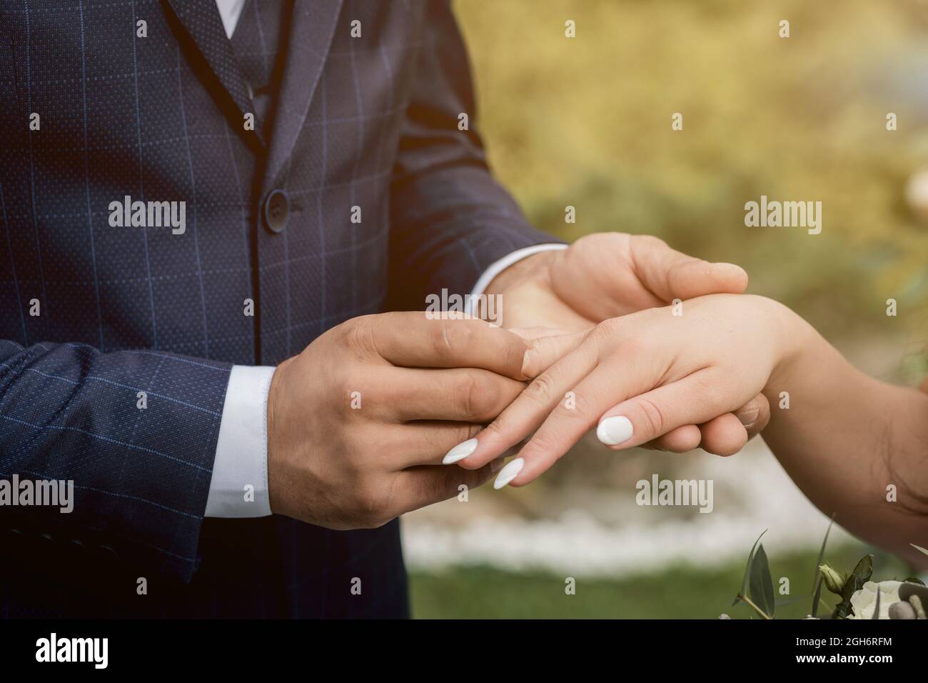 coppia che scambiano gli anelli di nozze durante la loro cerimonia nuziale all'aperto. Scatto corto dello sposo che mette un anello di nozze sul dito della sposa. Foto Stock