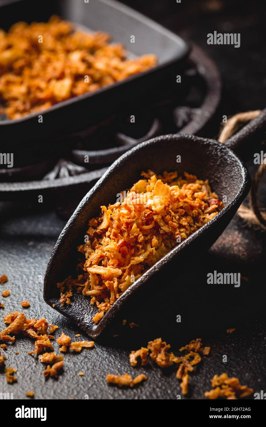 Cipolle fritte fatte in casa in una tazza da cucina in ferro con padella nera su sfondo nero Foto Stock