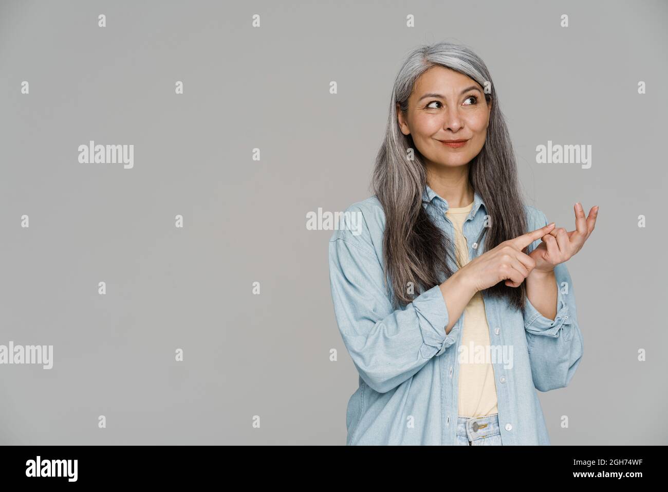 Pensare donna dai capelli bianchi sorridendo e contando sulle dita isolate sopra il muro grigio Foto Stock
