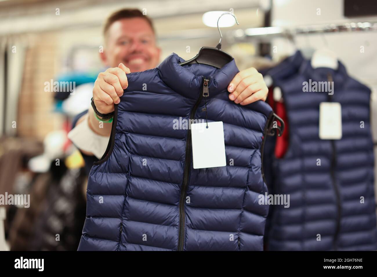 Uomo sorridente che tiene il nuovo caldo giubbotto in primo piano del negozio Foto Stock