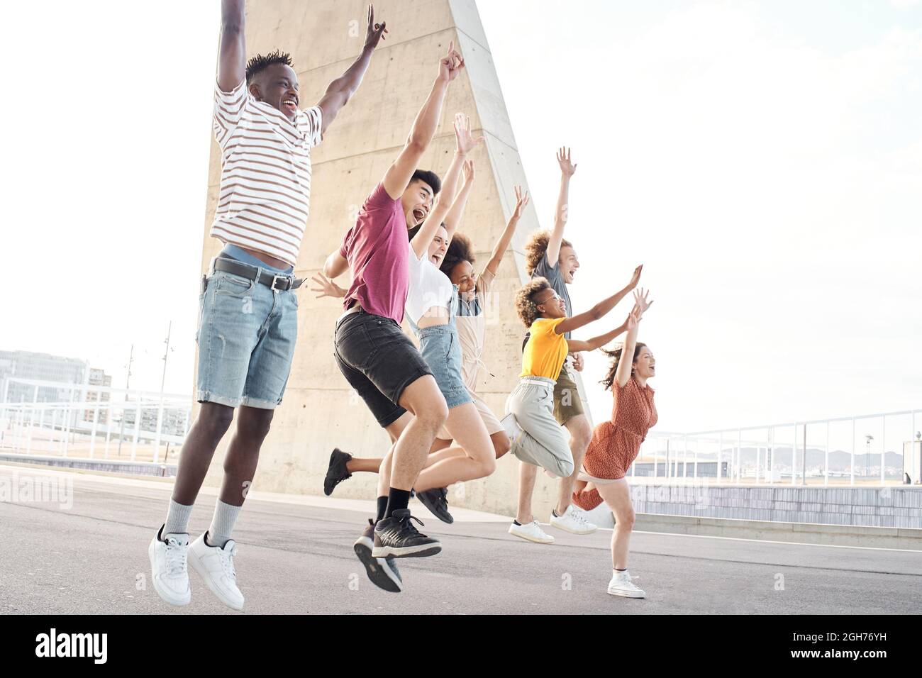 Vista laterale ritratto di gruppo di felici amici multietnici divertirsi. Giovani studenti che saltano fuori dall'università. Foto Stock