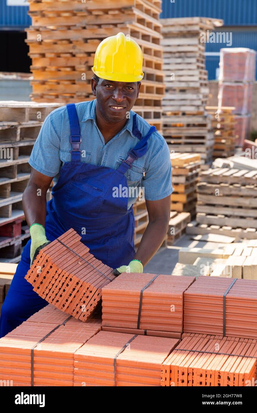 Costruttore maschile che trasporta mattoni in magazzino all'aperto Foto Stock