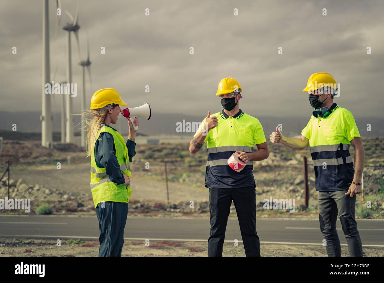 La donna ingegnere grida su un megafono. Lavoratori esperti con maschera protettiva, facendo ok segno, pollice in su con le dita. Centrale elettrica. Foto Stock