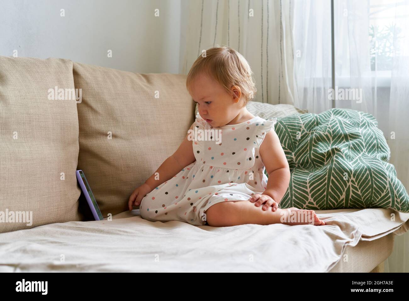 Adorabile bambina in abito guardando cartoni animati su smartphone, seduto sul divano mentre la mamma è assente Foto Stock