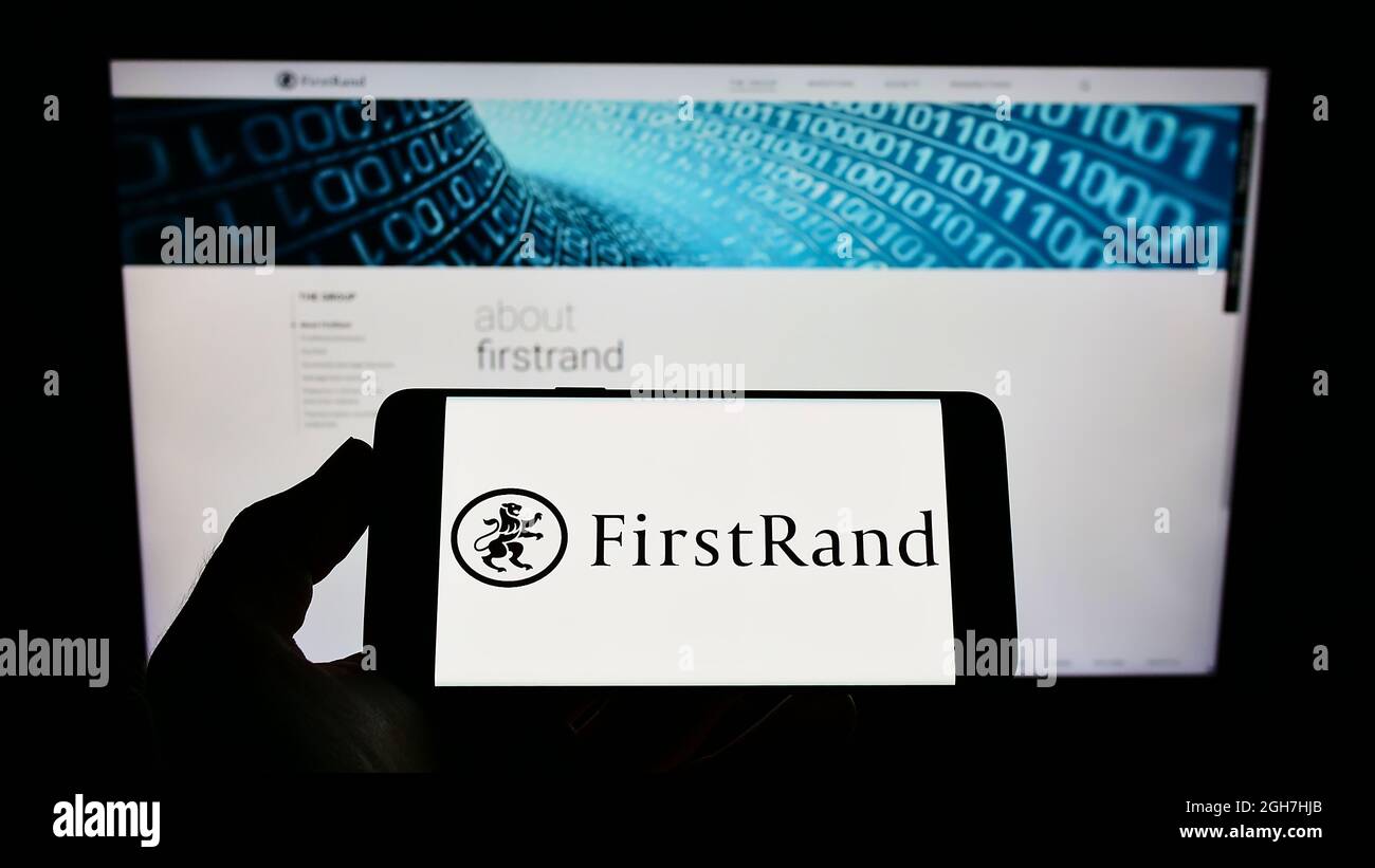 Persona che tiene lo smartphone con il logo della banca sudafricana FirstRand Limited sullo schermo di fronte al sito web. Mettere a fuoco sul display del telefono. Foto Stock
