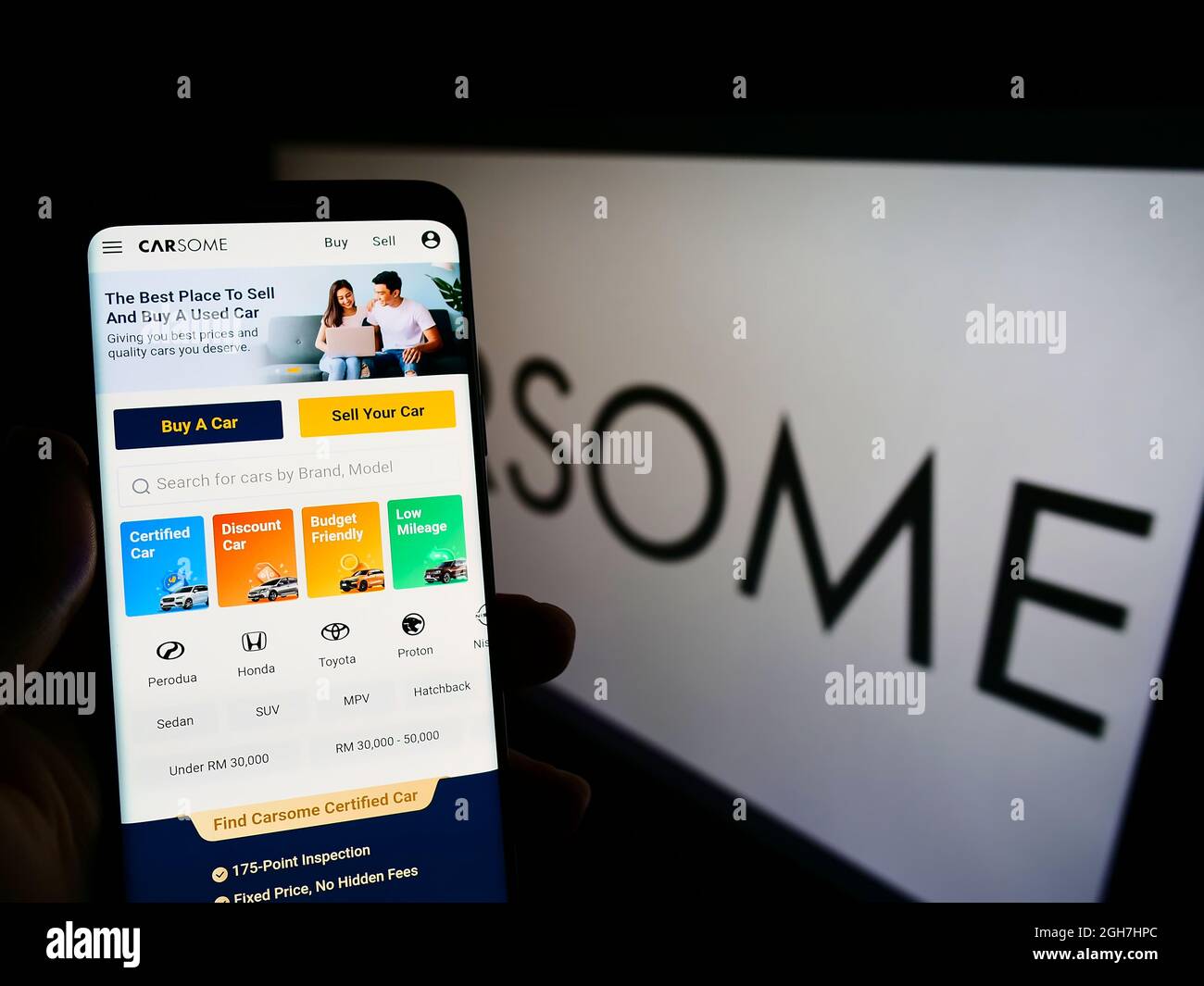 Persona che tiene smartphone con sito web della società malese piattaforma auto usate Carsome Group sullo schermo con logo. Concentrarsi sul centro del display del telefono. Foto Stock