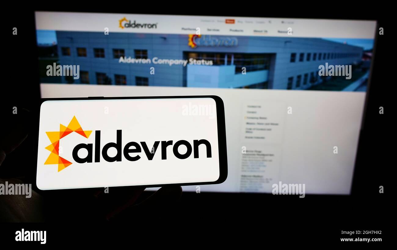 Persona che tiene il cellulare con il logo della società di biotecnologia americana Aldevron LLC sullo schermo di fronte al sito web aziendale. Mettere a fuoco sul display del telefono. Foto Stock