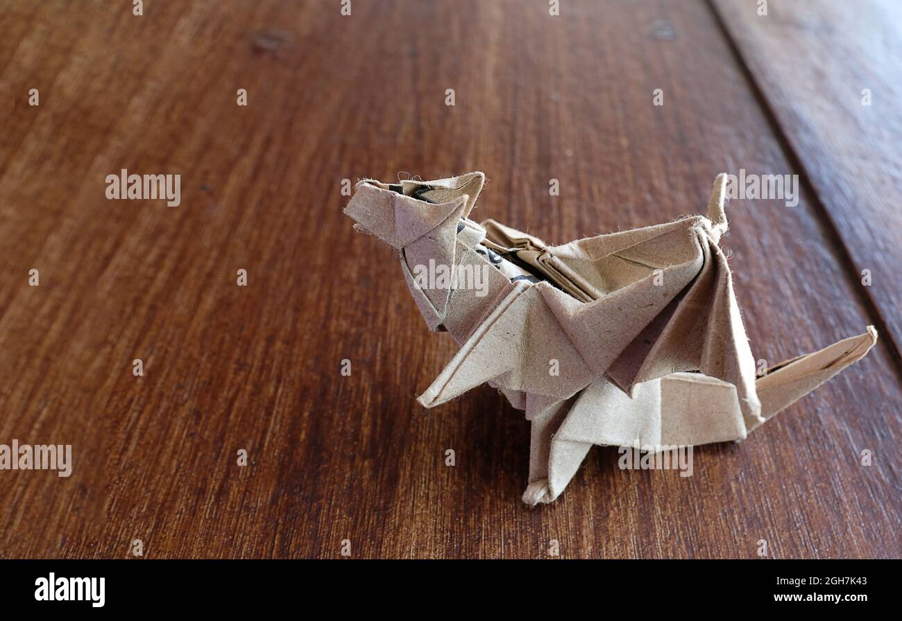 Un modello di drago origami realizzato in carta marrone pesante, su un piano in legno. Foto Stock
