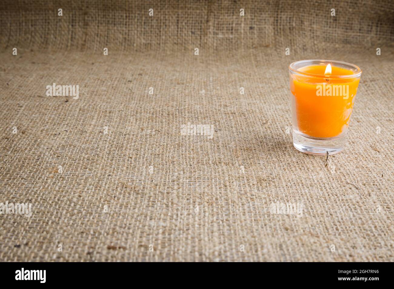 Candela arancione in un bicchiere con fondo marrone in tessuto di sackcloth Foto Stock