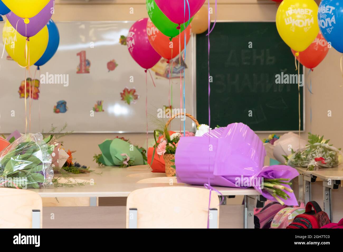 Lezione di scuola il 1 settembre senza studenti con palloncini colorati e fiori su scrivanie sullo sfondo del consiglio di scuola. Le iscrizioni Foto Stock