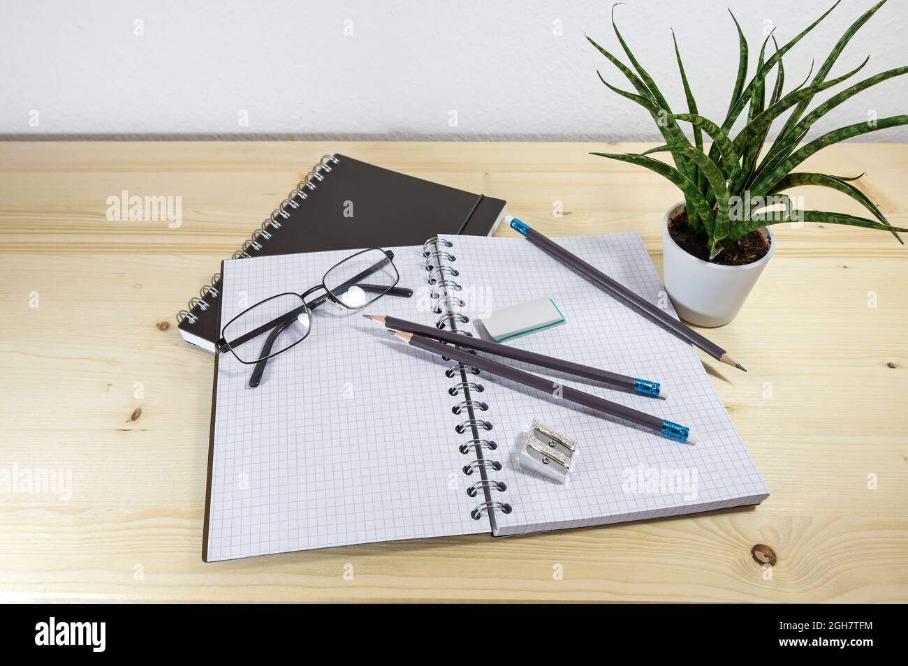 Scrivania da ufficio o studio con un notebook a spirale aperta, matite, occhiali e forniture su un tavolo di legno, spazio per la copia, fuoco selezionato, profondità di campo stretta Foto Stock