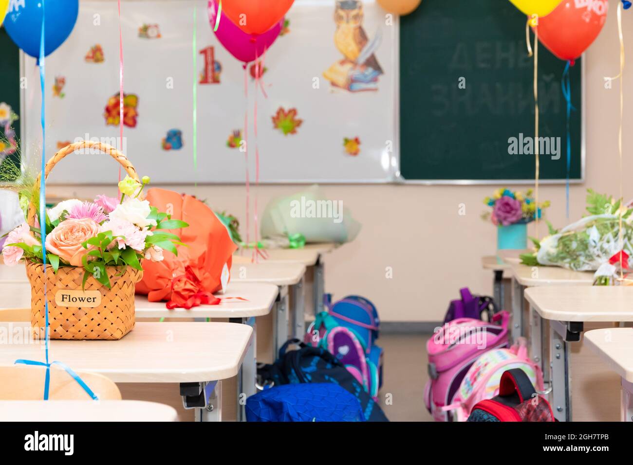 Lezione di scuola il 1 settembre senza studenti con palloncini colorati e fiori su scrivanie sullo sfondo del consiglio di scuola. Le iscrizioni Foto Stock