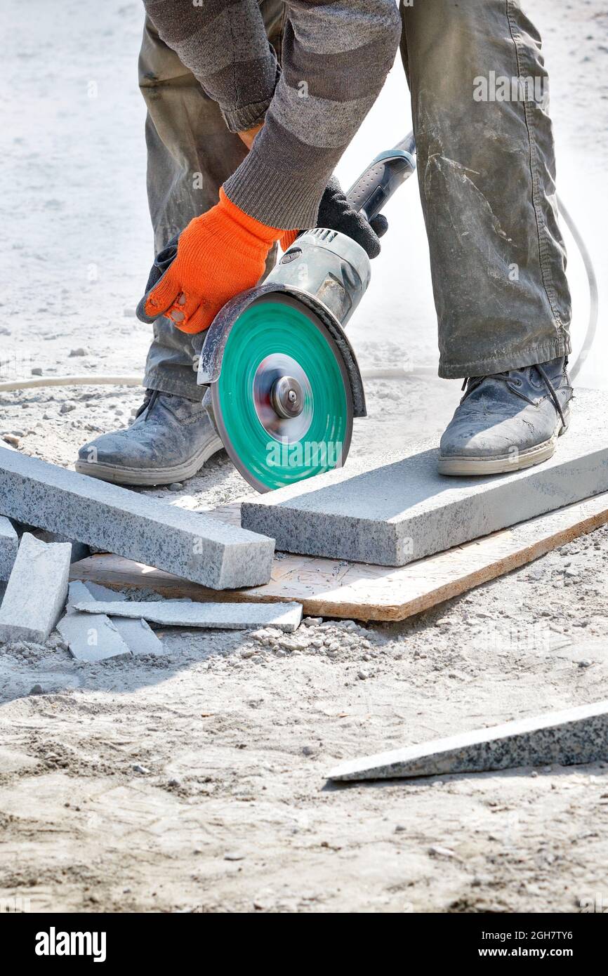 Un costruttore usa un disco di taglio del diamante e del macinacaffè per tagliare i blocchi di granito. Immagine verticale. Foto Stock