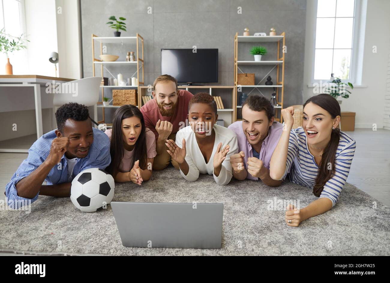 Gruppo di giovani amici entusiasti che si trovano a casa e guardano la partita di calcio su un computer portatile Foto Stock